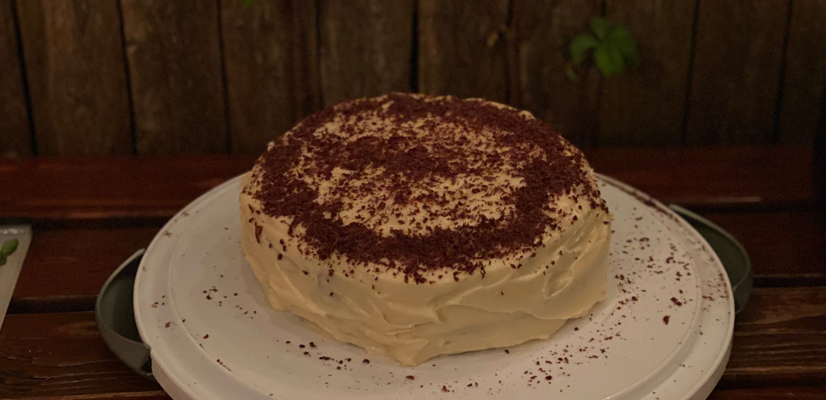 image of a cake on a plate - somewhat sloppily decorate, with cream cheese frosting and poorly arranged chocolate shavings